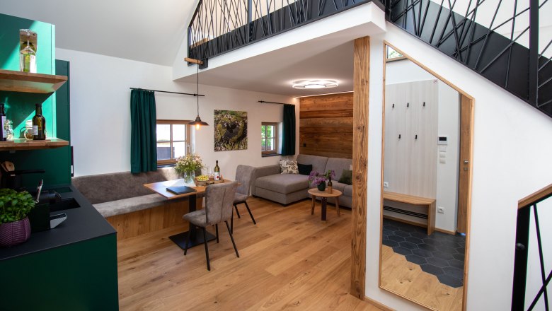 Modern apartment with wooden floor, gray sofa, dining table and open gallery.