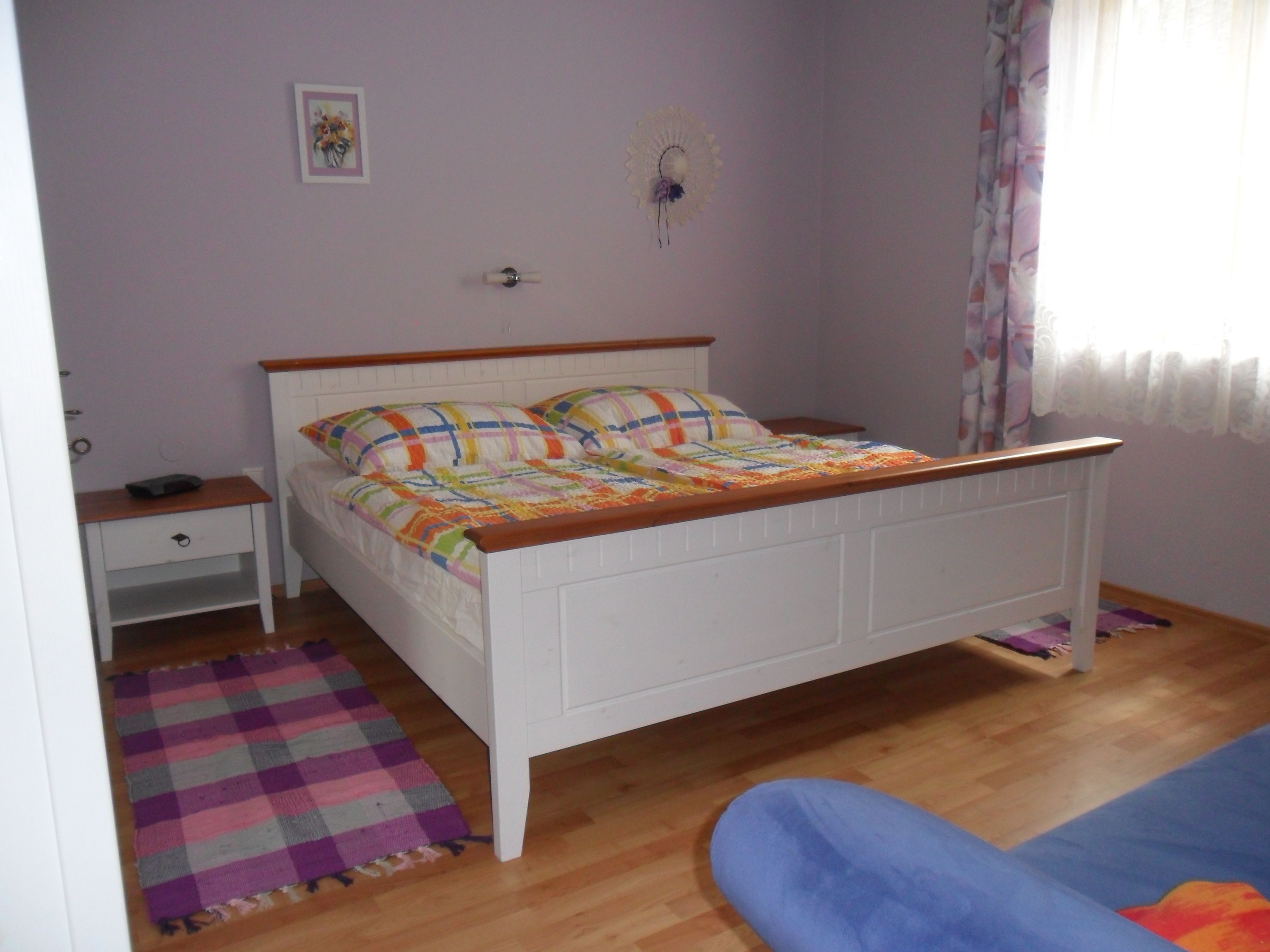 A bedroom with a white bed, colorful comforters, a bedside table and a window with curtains.