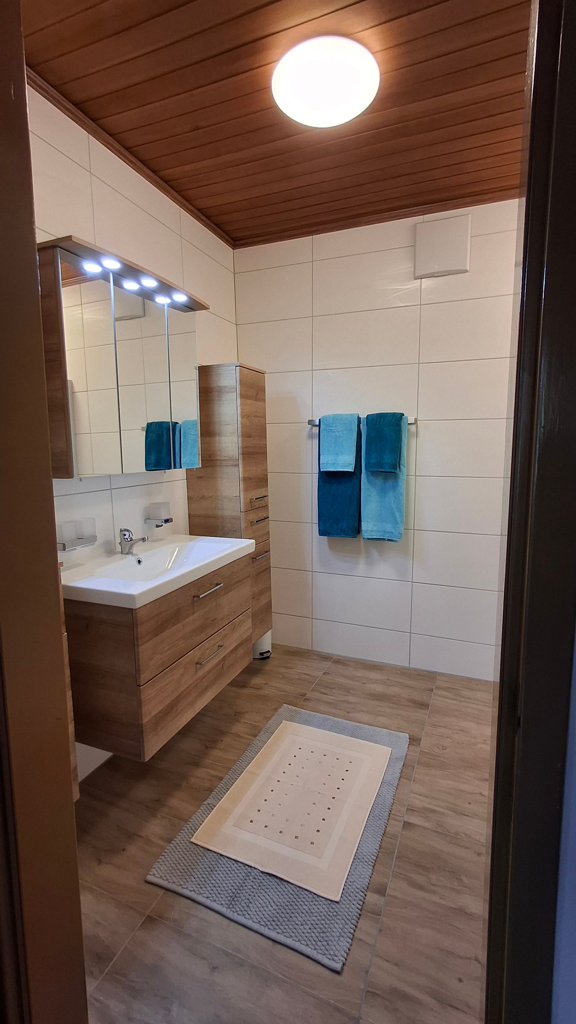 Modern bathroom with wooden ceiling, washbasin, mirror, towels and carpet.