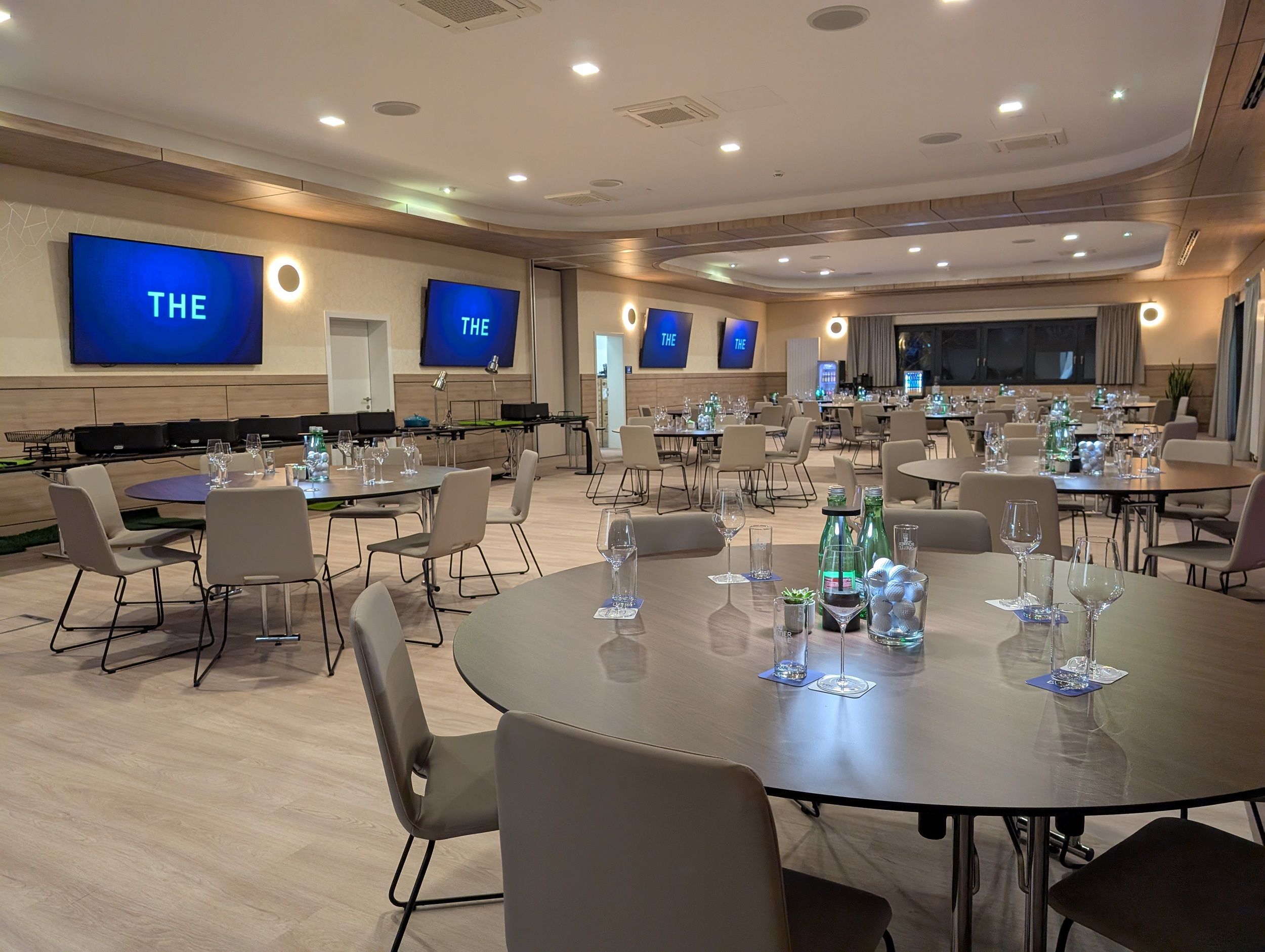 Modern seminar room with round tables, chairs and screens on the walls.