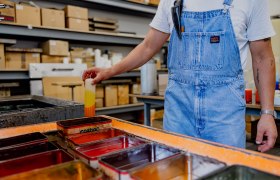 Person in dungarees dips candle in paint bath.