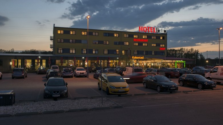 Evening shot of a hotel with parking lot and cars in front of it.