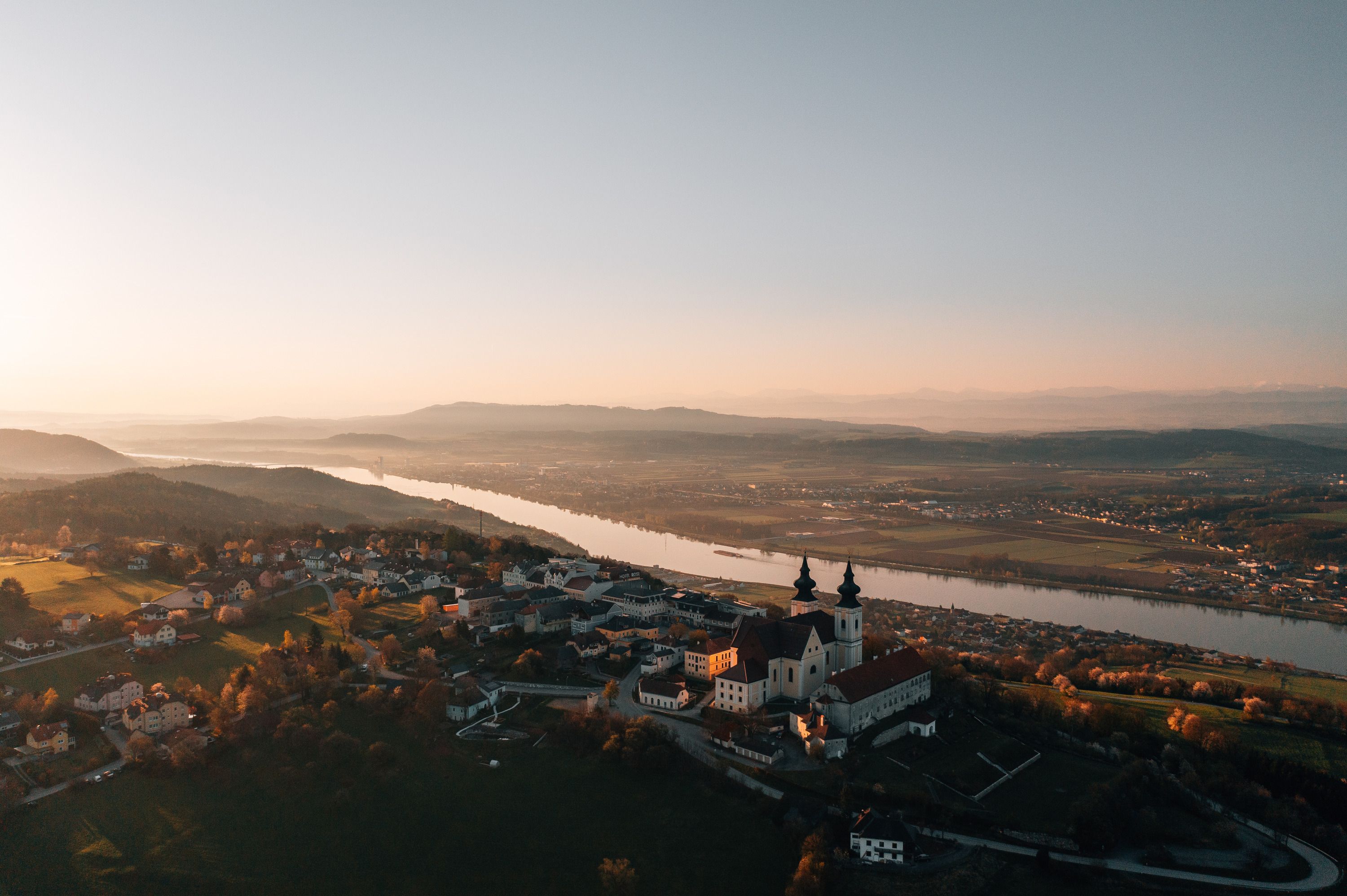 Aerial view of a church at sunset, surrounded by river and landscape.