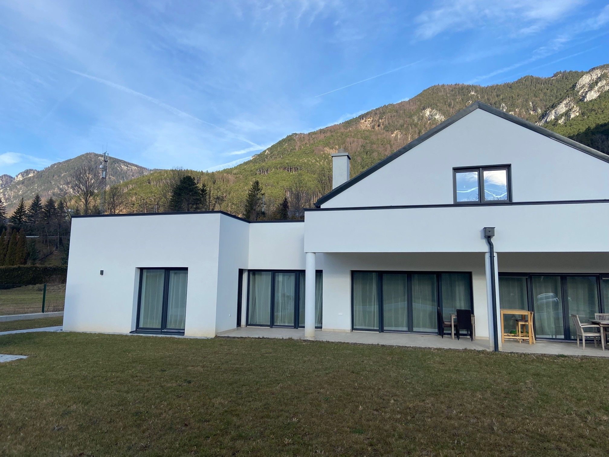 Modern white house with large windows against a mountain backdrop.