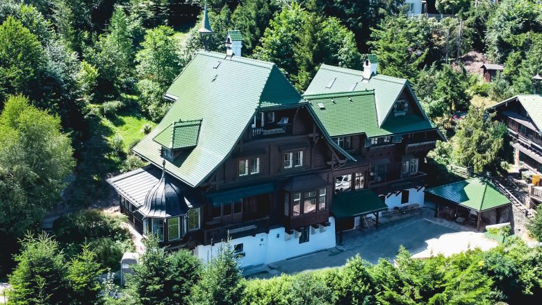 Aerial view of a large villa with a green roof, surrounded by trees.