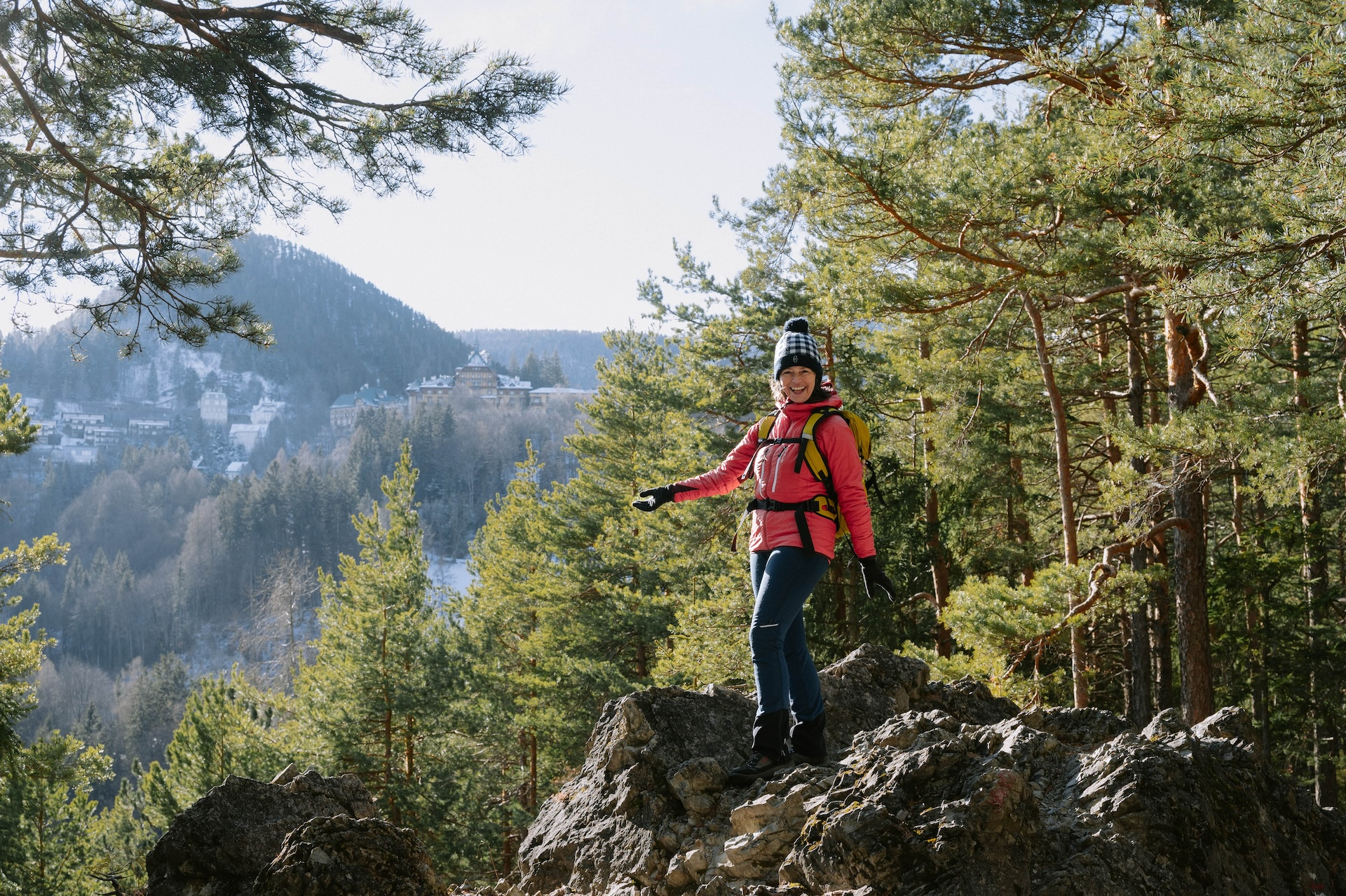 Person in pink jacket walking on a rocky path in the forest with mountains in the background.