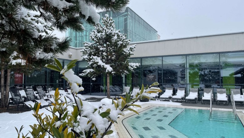 Outdoor area of Therme Linsberg Asia with snow-covered trees and sun loungers, next to a pool.