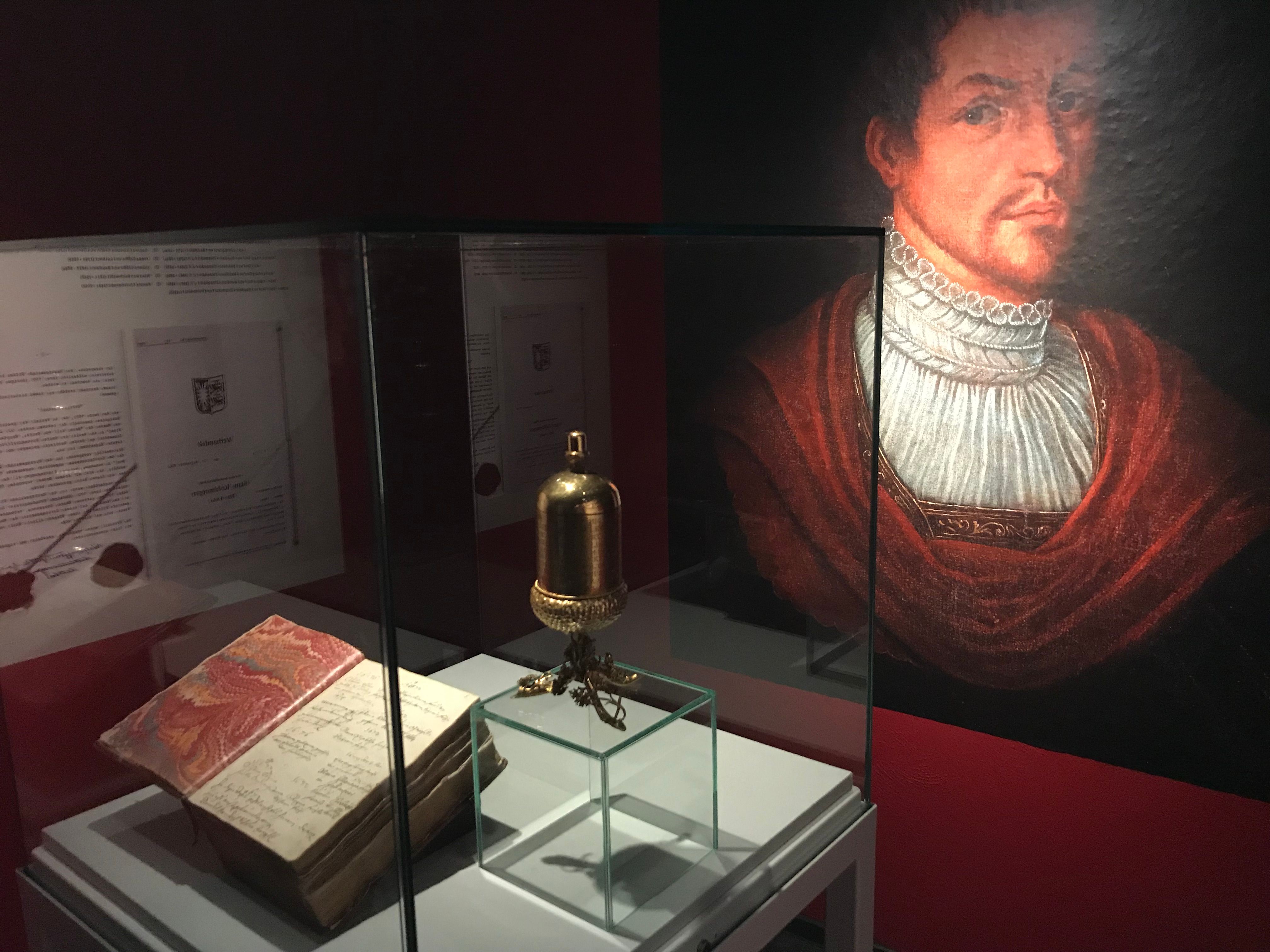 Exhibition with a golden cup, an old book and a portrait in a museum.