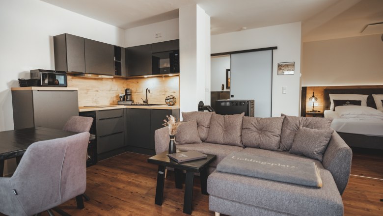 Modern living area with gray sofa, kitchenette and dining table.