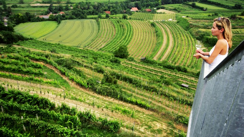 Woman with a wine glass looks out over green vineyards from a vantage point.