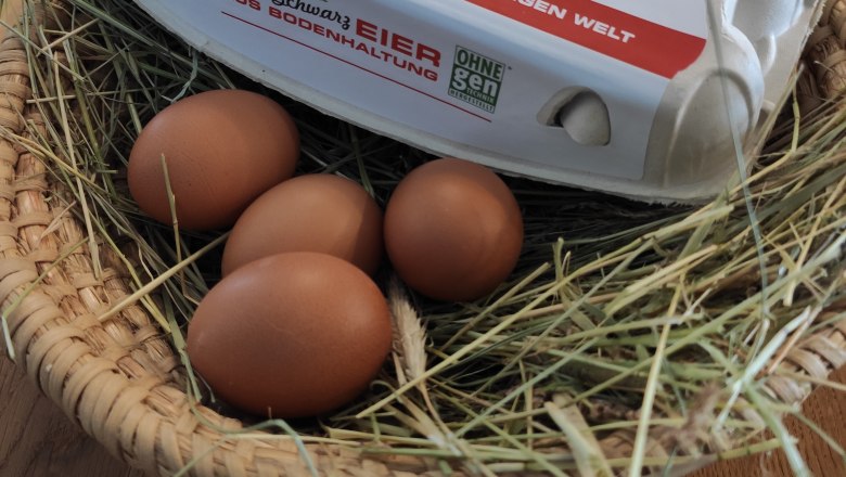 An egg carton labeled 'Eierhof Schwarz' lies on a basket of straw and brown eggs.