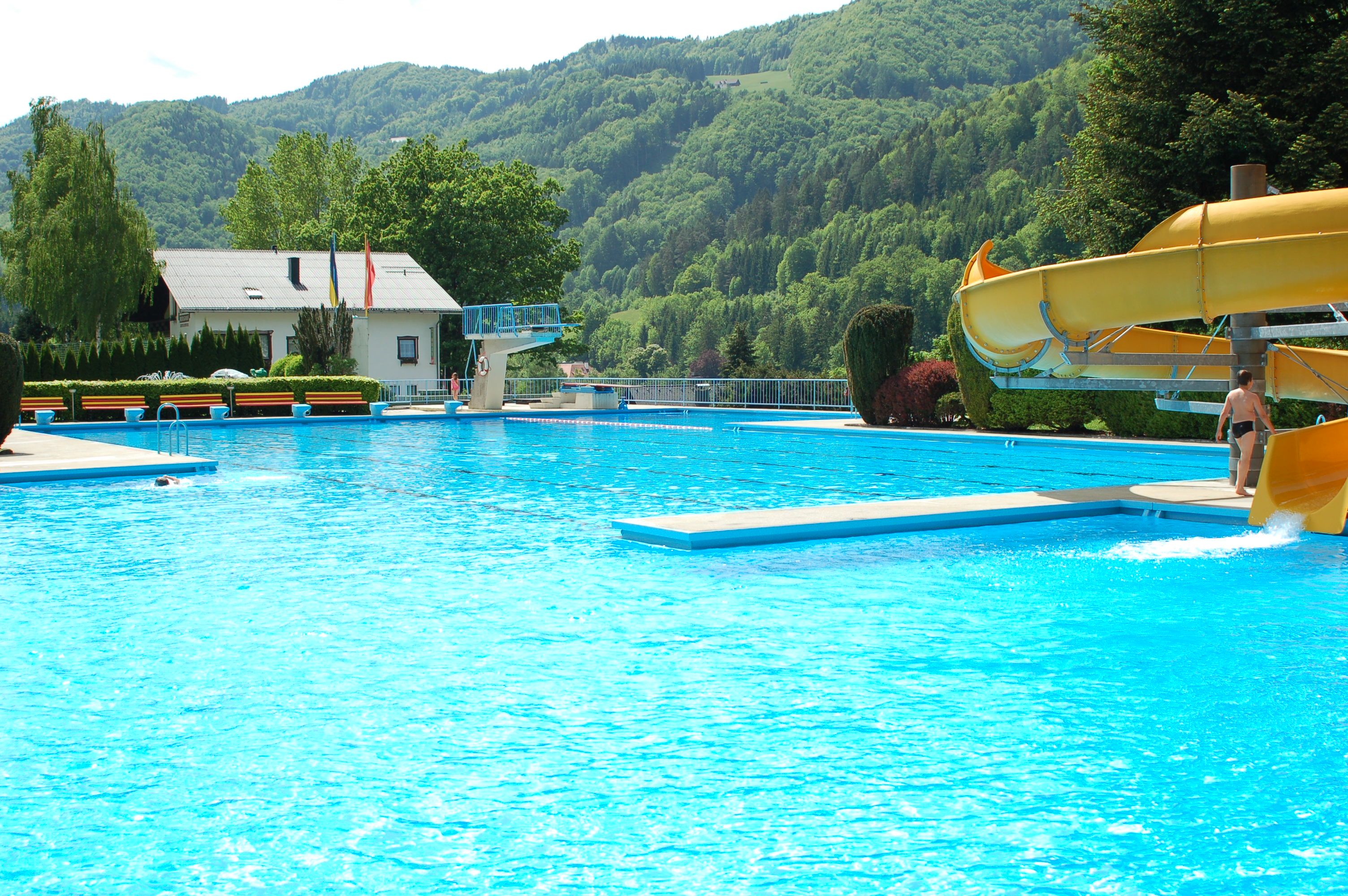 An outdoor pool with slide, diving board and surrounding mountains.