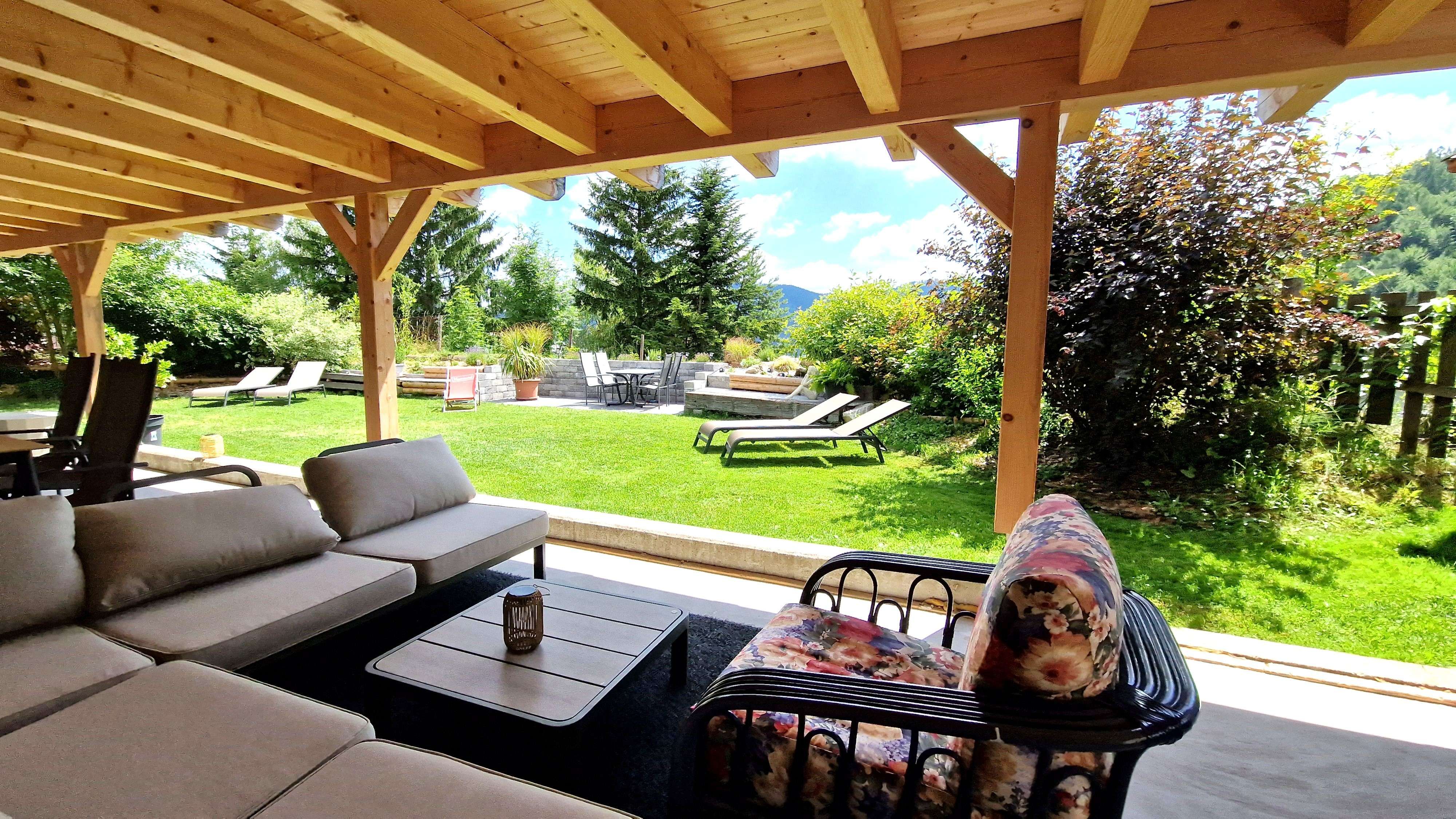 A covered patio with seating and a view of a garden with lounge chairs and trees.