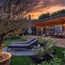 A modern chalet with terrace and sun loungers in the garden at sunset.