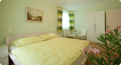 A light green bedroom with a double bed, white furniture and a picture on the wall.