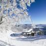 Winter landscape with chairlift station, snow-covered trees and mountains in the background.