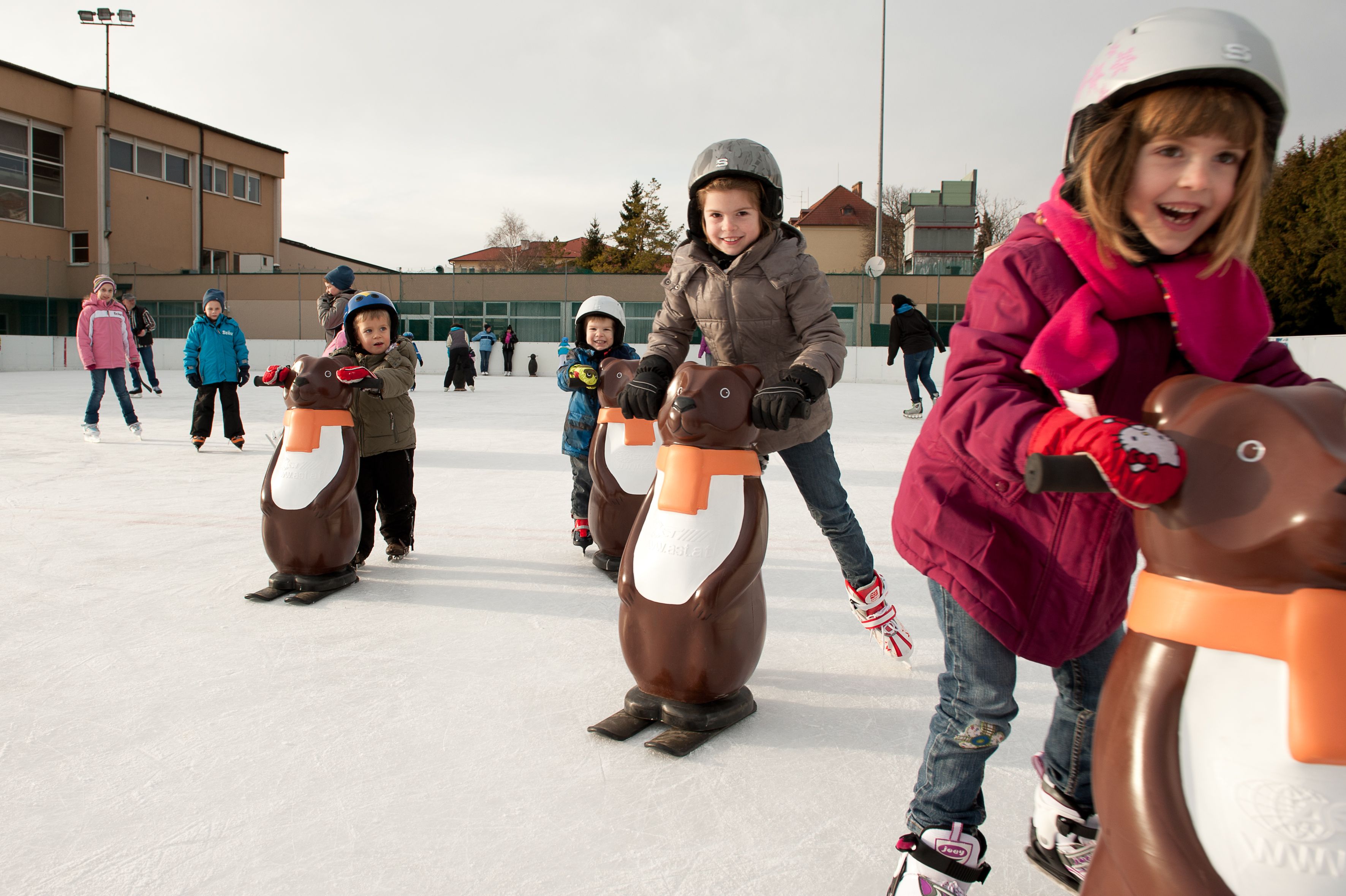 Children skating with penguin aids on an ice rink.
