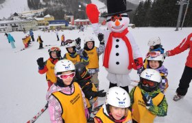Children in ski gear pose with a snowman on a ski slope.