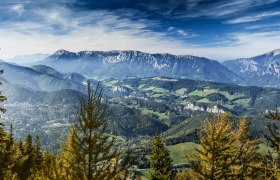 Panoramic view from the Sonnwendstein of wooded hills and mountains under a blue sky.