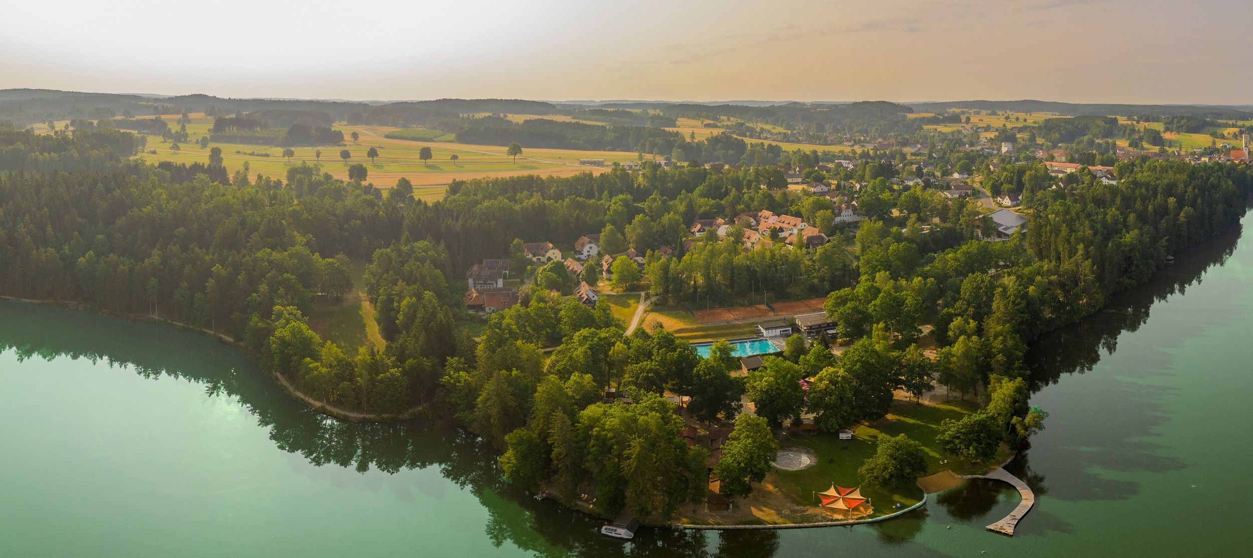 Aerial view of a lake with surrounding forest and buildings.