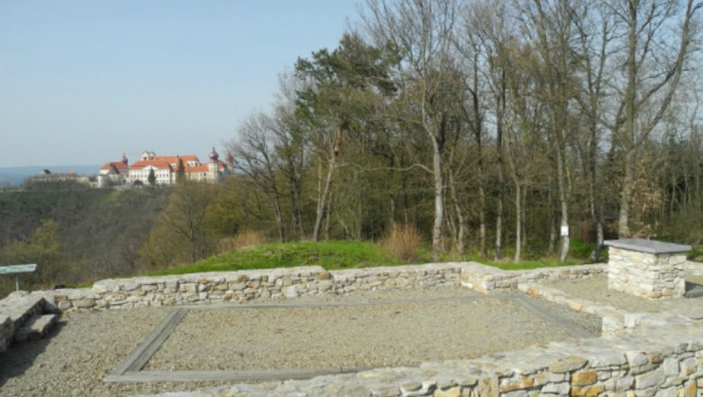 Ruins of an old stone wall with a castle in the background on a hill.