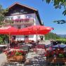 A traditional inn with a terrace, red parasols and flower boxes against a clear blue sky.