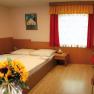A cozy room with a double bed, red curtains, a table with chairs and a bouquet of sunflowers in the foreground.