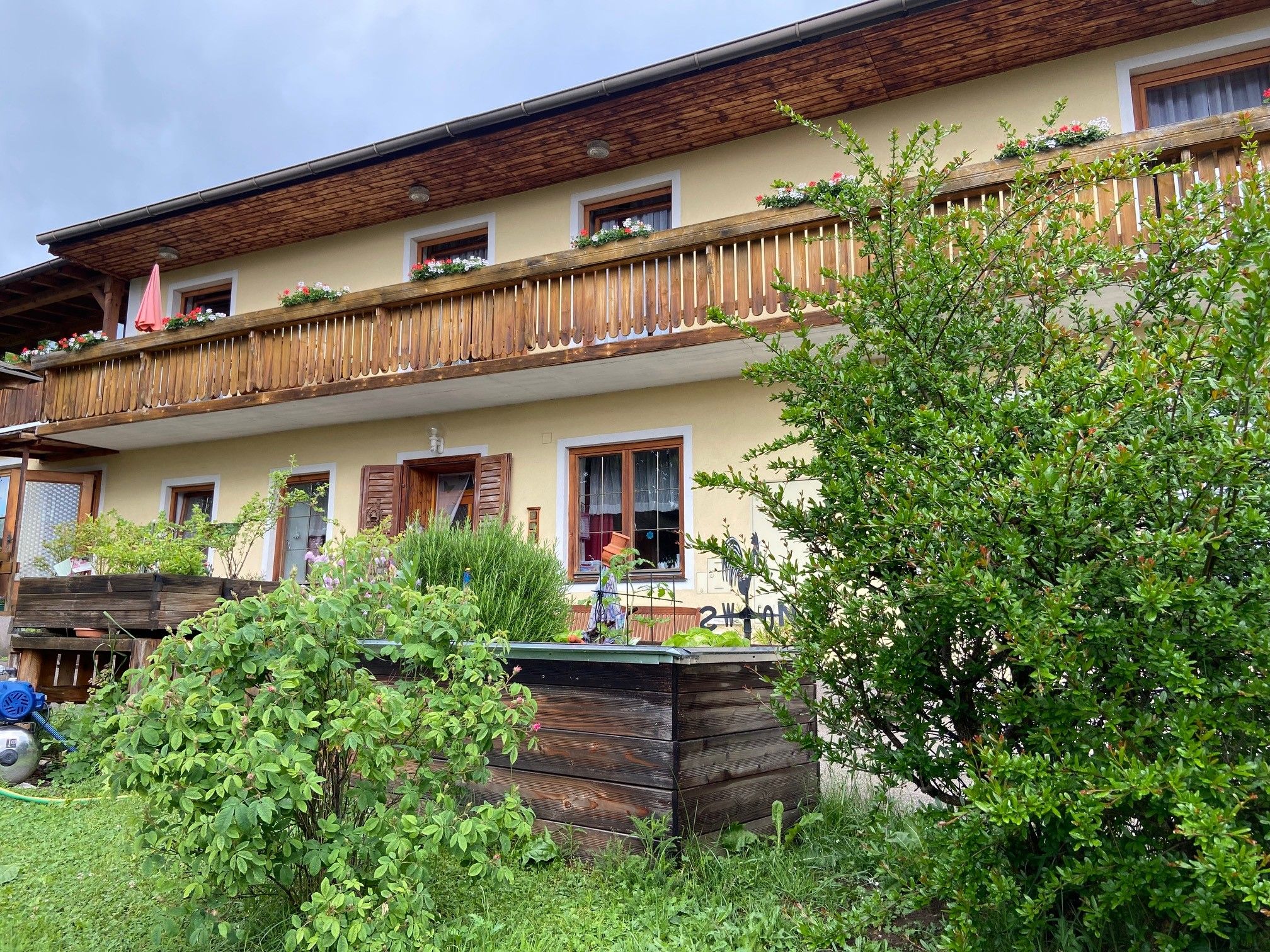 Two-storey house with wooden balcony and garden.