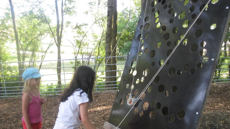 Two children playing on a perforated wall outdoors.