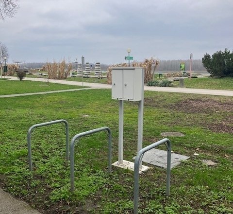 E-bike charging stations on a meadow with bike racks and a path in the background.