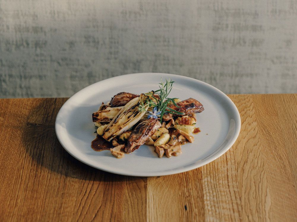 A plate of venison saltimbocca, gnocchi and herb garnish on a wooden table.