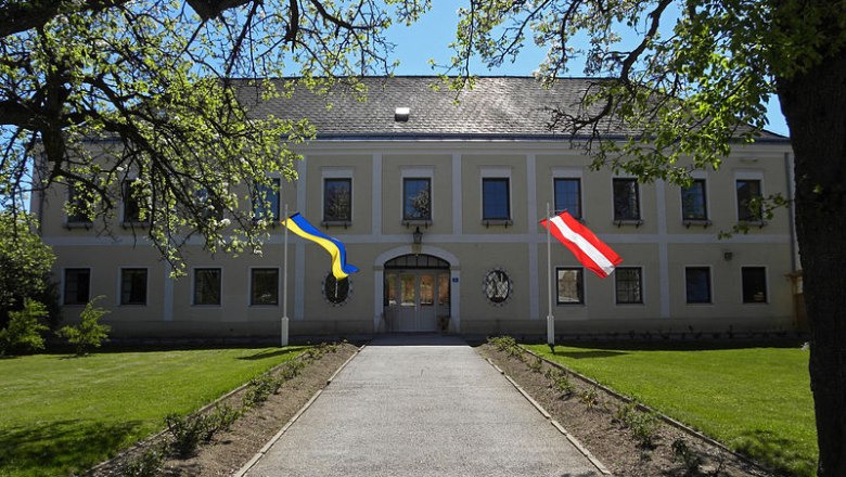 Hochwolkersdorf Castle with two flags, surrounded by trees and lawn.