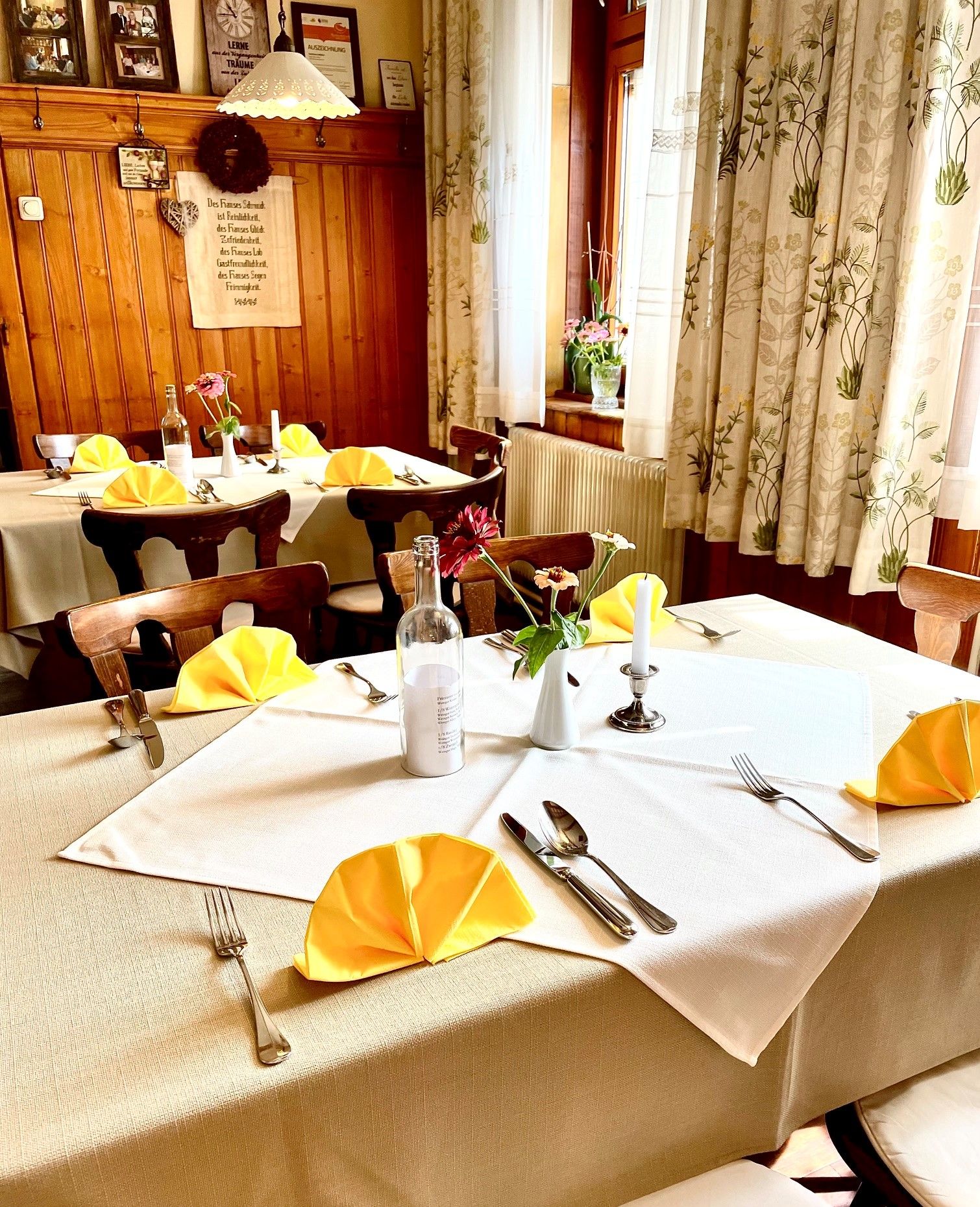 An interior view of a cozy inn with wooden walls, set tables with yellow napkins, and flowers.