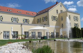 Large yellow building with red roof tiles, fountain and pavilion in the foreground.