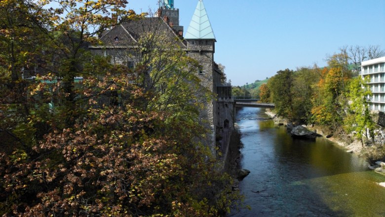 River with fall trees and buildings in the background.