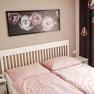 Bedroom with pink bed linen, white bed frame and flower picture on the wall.