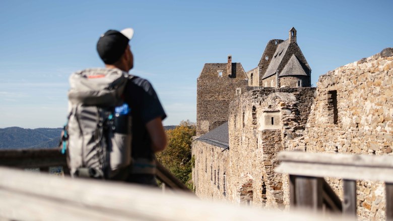 A hiker with a rucksack looks at the ruins of Aggstein Castle on a sunny day.