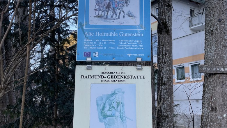 Two signs on a tree, one for the Forest Farmers' Museum and one for the Raimund Memorial.