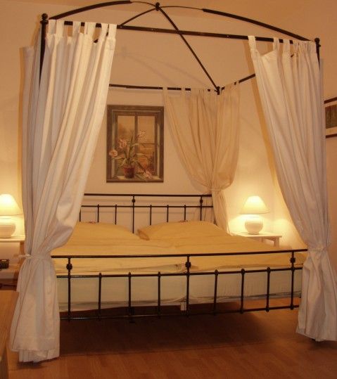 A four-poster bed with white curtains in a cozy bedroom, illuminated by two bedside lamps.