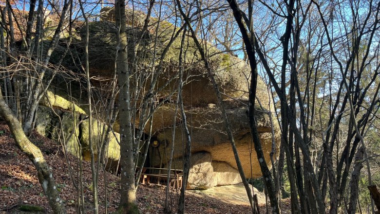 Rock formation in the forest with bare trees and leaves on the ground.
