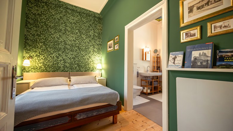 Cozy bedroom with green patterned wallpaper, double bed and adjoining bathroom.