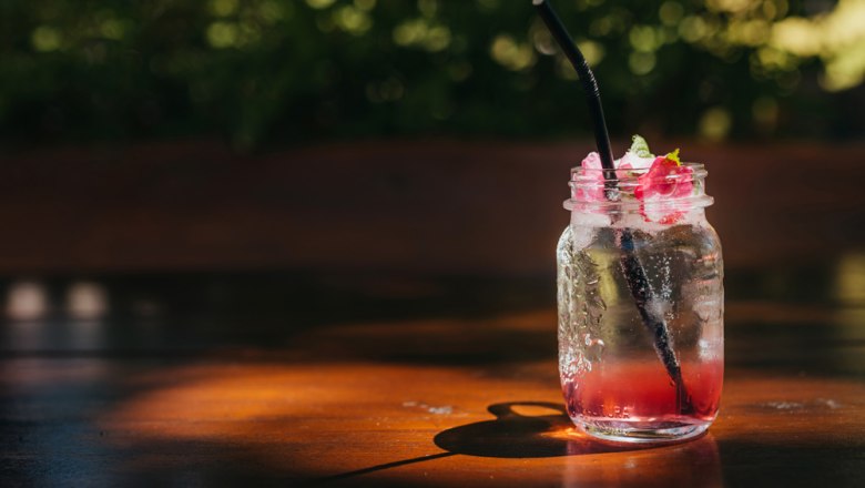 A glass with a red drink and a black straw on a wooden table.