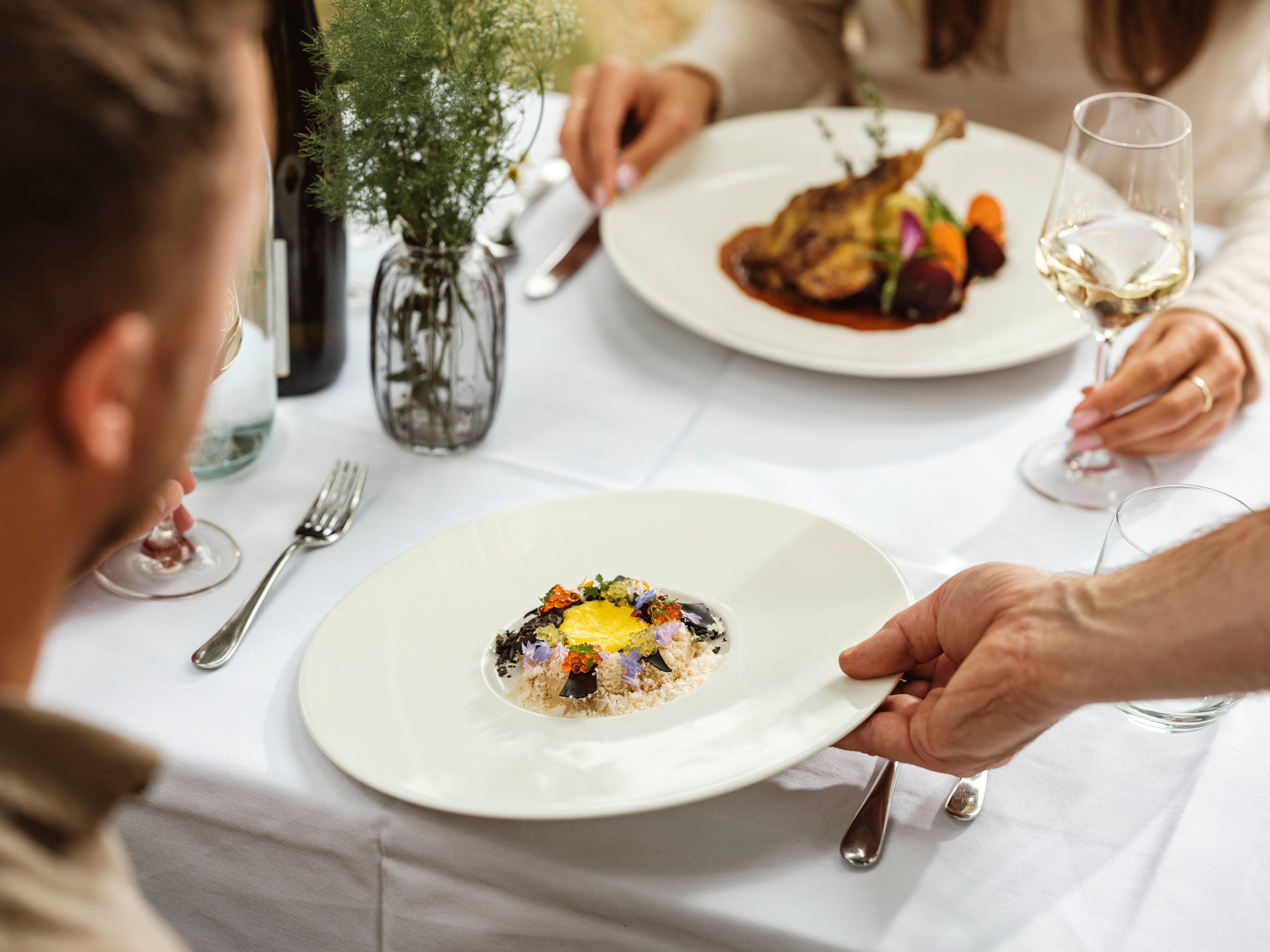An elegant restaurant meal with two people sitting at a table. A plate with an artfully arranged dish is served.