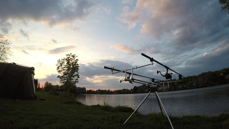Fishing rods on a stand on the lakeshore at sunset.