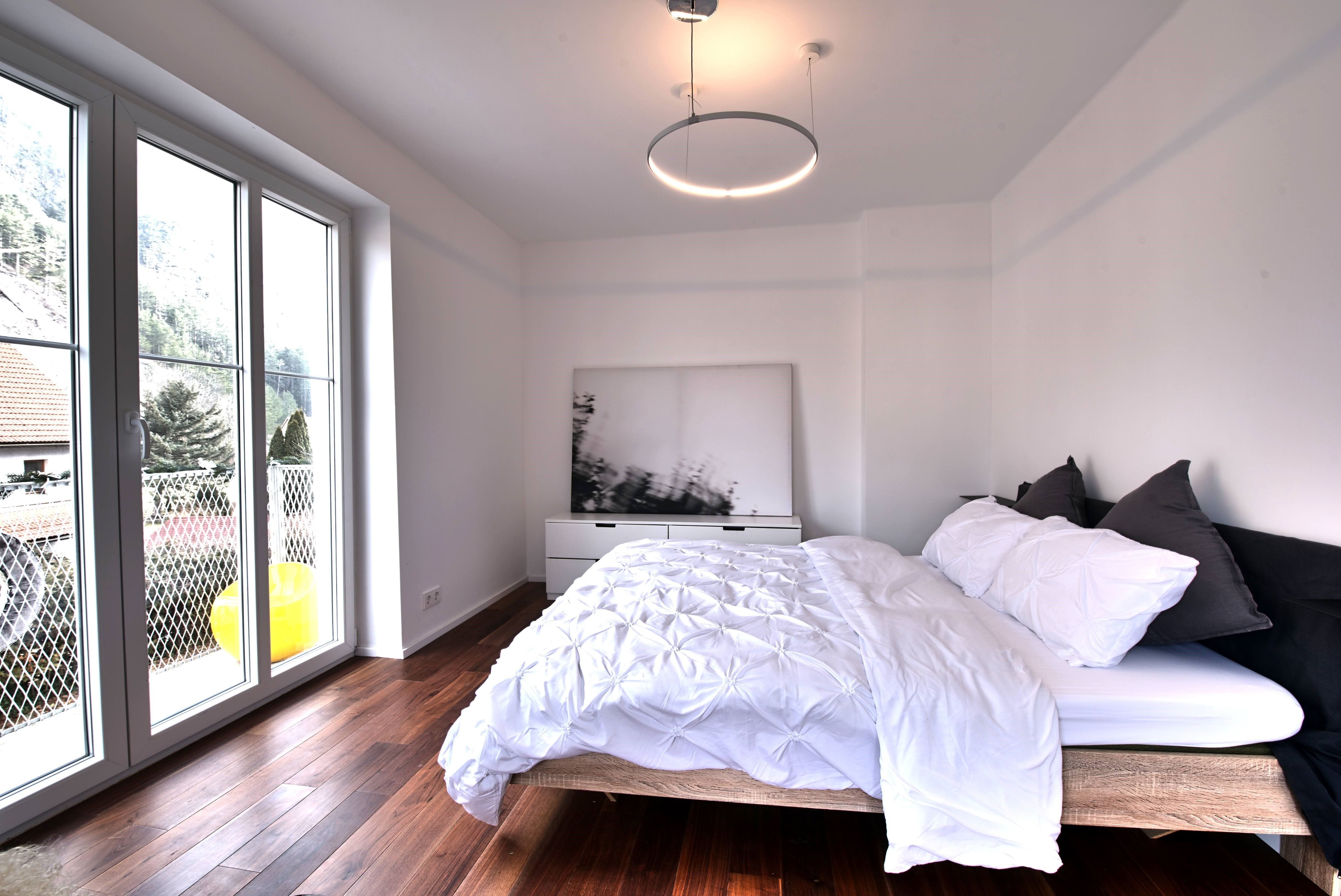 Modern bedroom with large window, wooden floor and double bed.