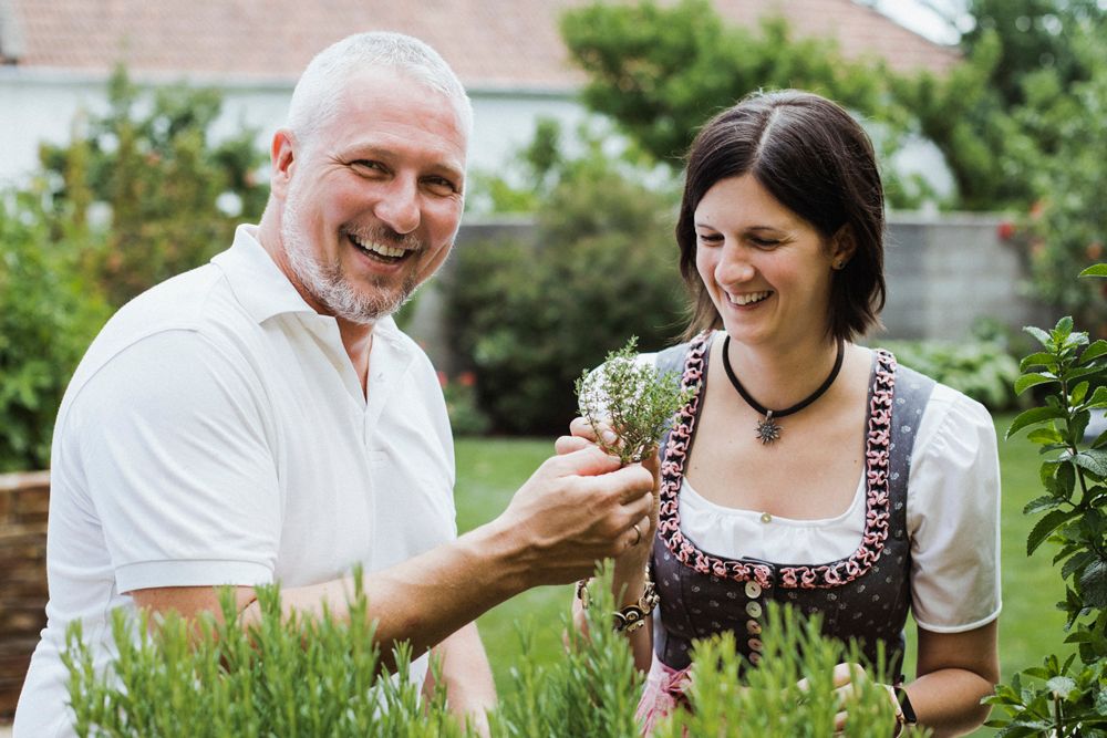 A man and a woman stand smiling in a garden looking at herbs.