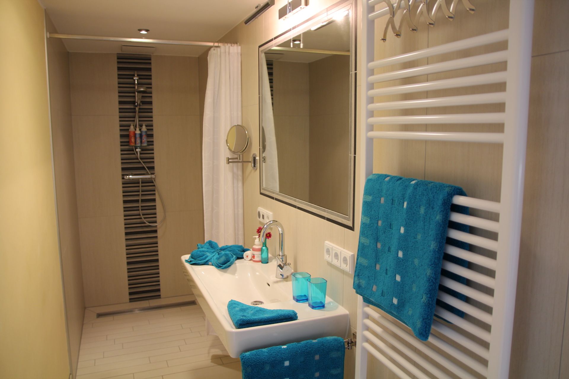Modern bathroom with shower, washbasin and blue towels.