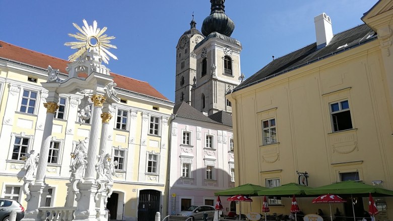 Historic square with baroque column, church and caf&eacute;.
