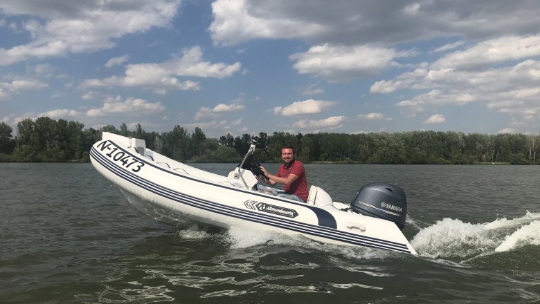 A man drives an inflatable boat with a Yamaha engine on a lake, surrounded by trees and under a cloudy sky.