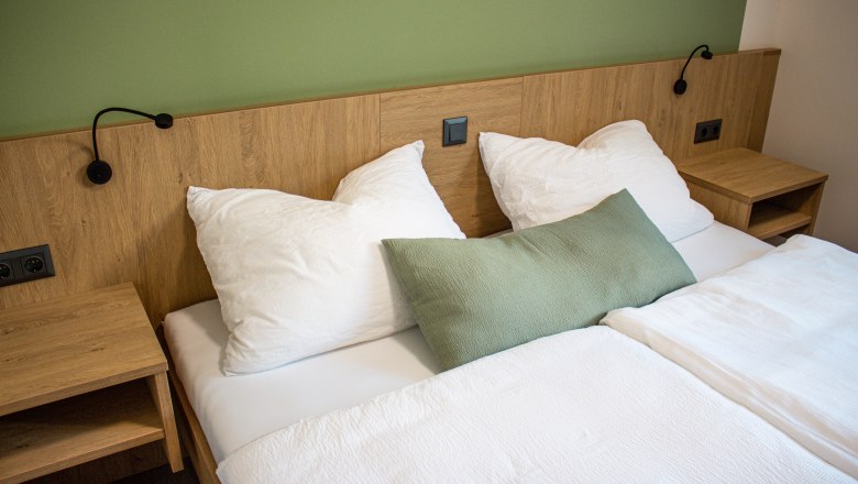 A double bed with white bed linen and a green wall in the background.